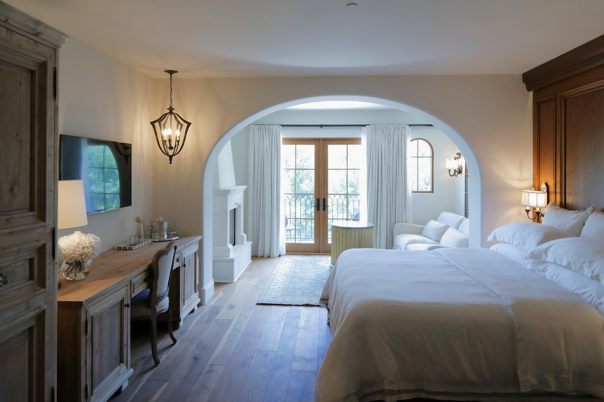 A wide view of a hotel room with a large bed, desk, TV, and fireplace.