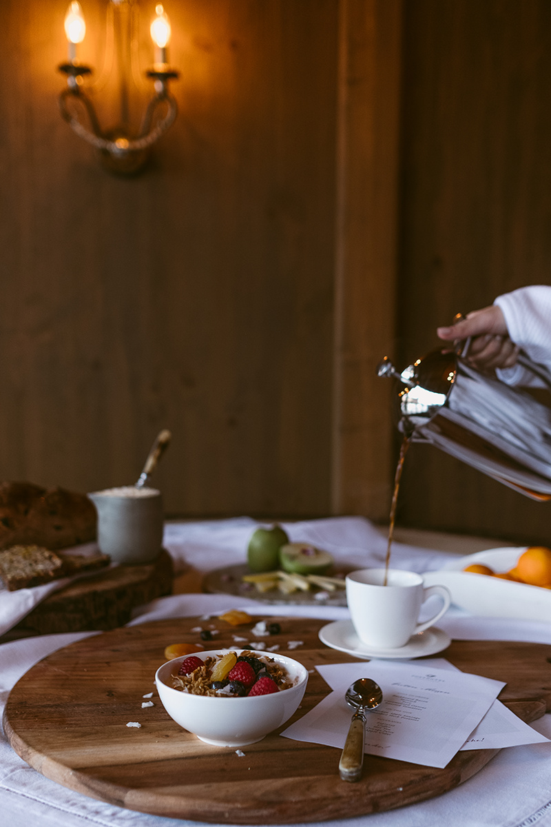 A person pouring coffee into a cup on a breakfast table with fruit and other breakfast items.