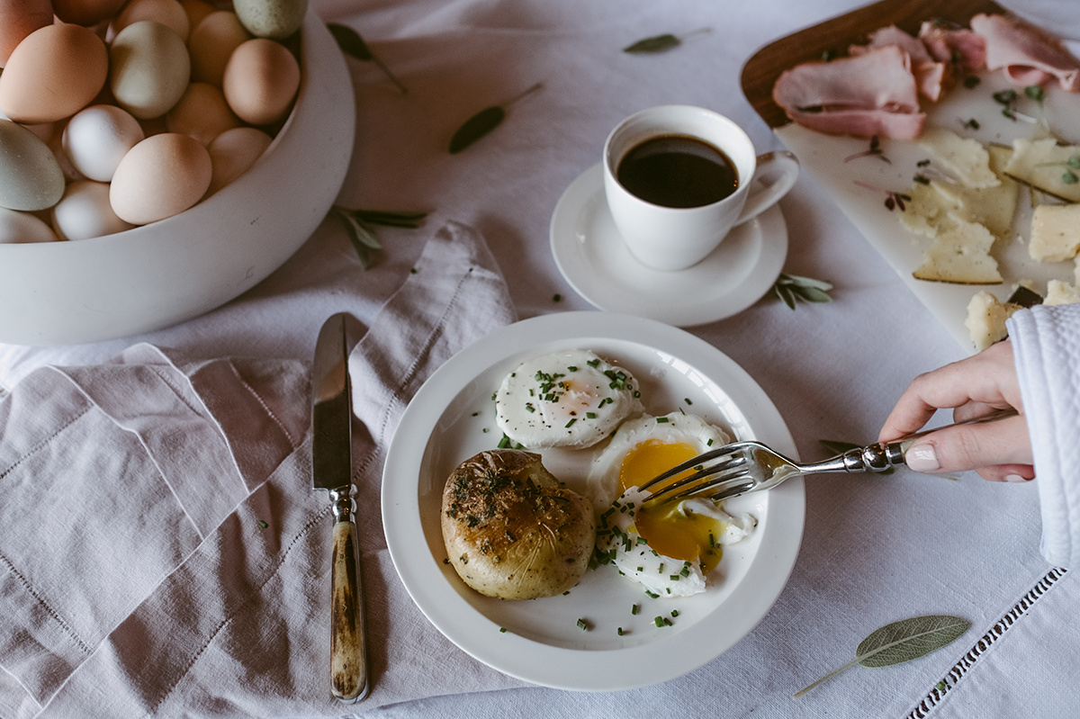 A breakfast table setting with eggs, coffee, meat, and cheese on a white tablecloth.