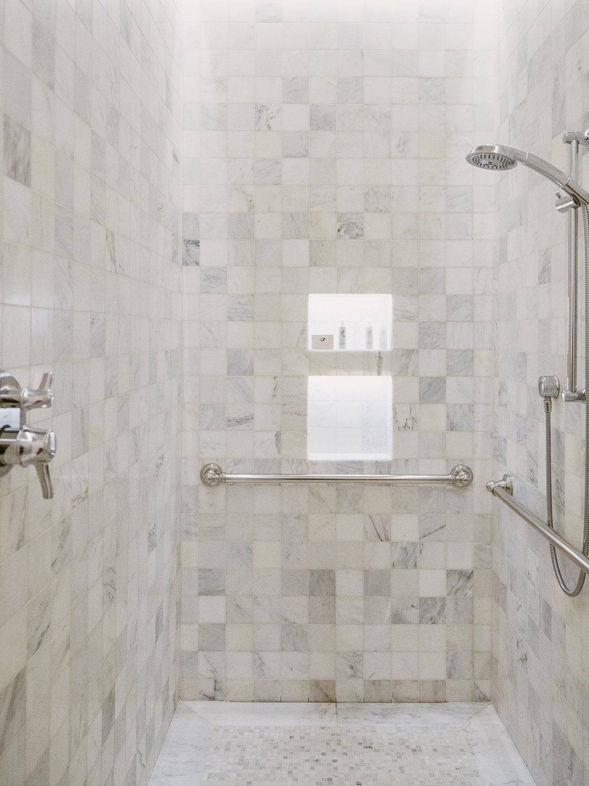 A marble-tiled shower with a grab bar, shower head, and rain showerhead.