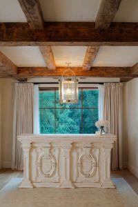 A serene spa reception area with a large window, beige curtains, a chandelier, and a decorative reception desk.